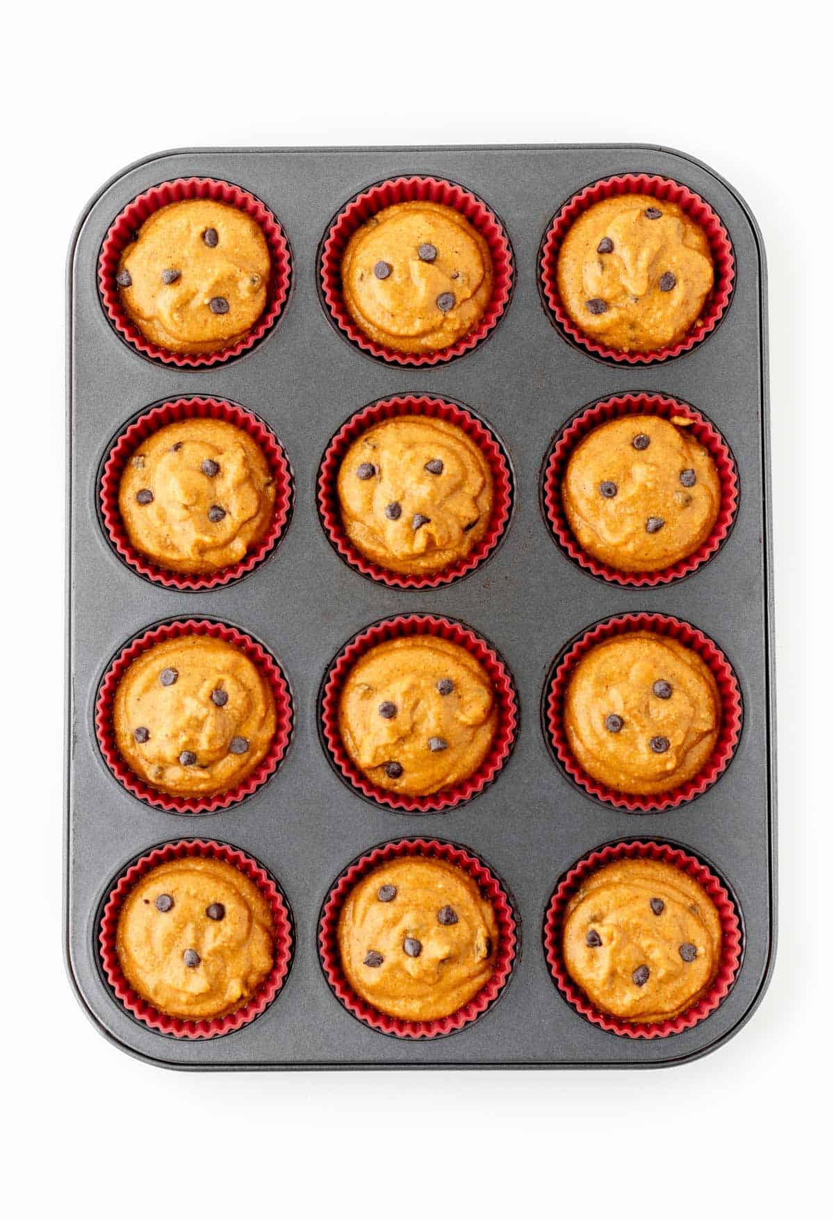 Pumpkin peanut butter muffin mixture spooned into muffin liners in a muffin pan.