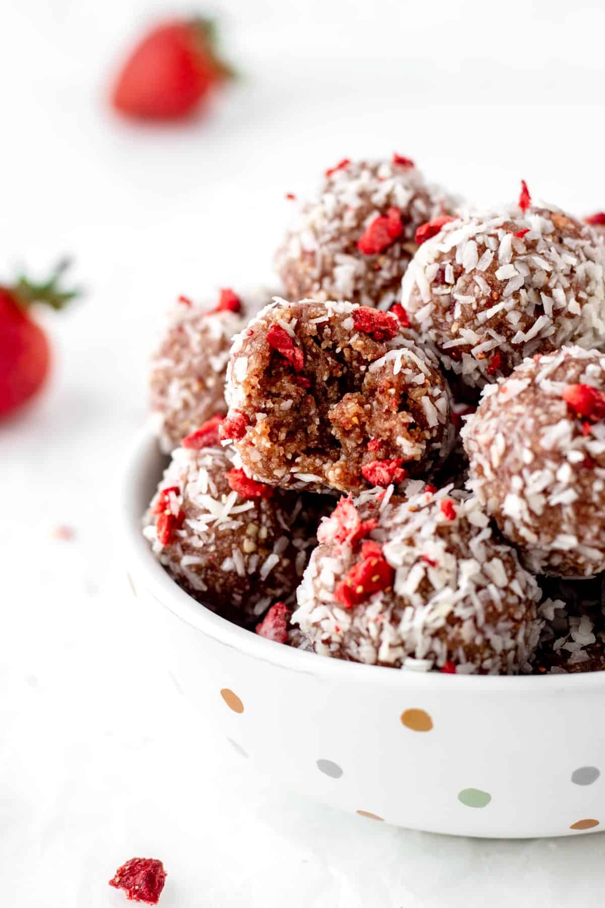 A half bitten strawberry bliss ball in a bowl with more of them.