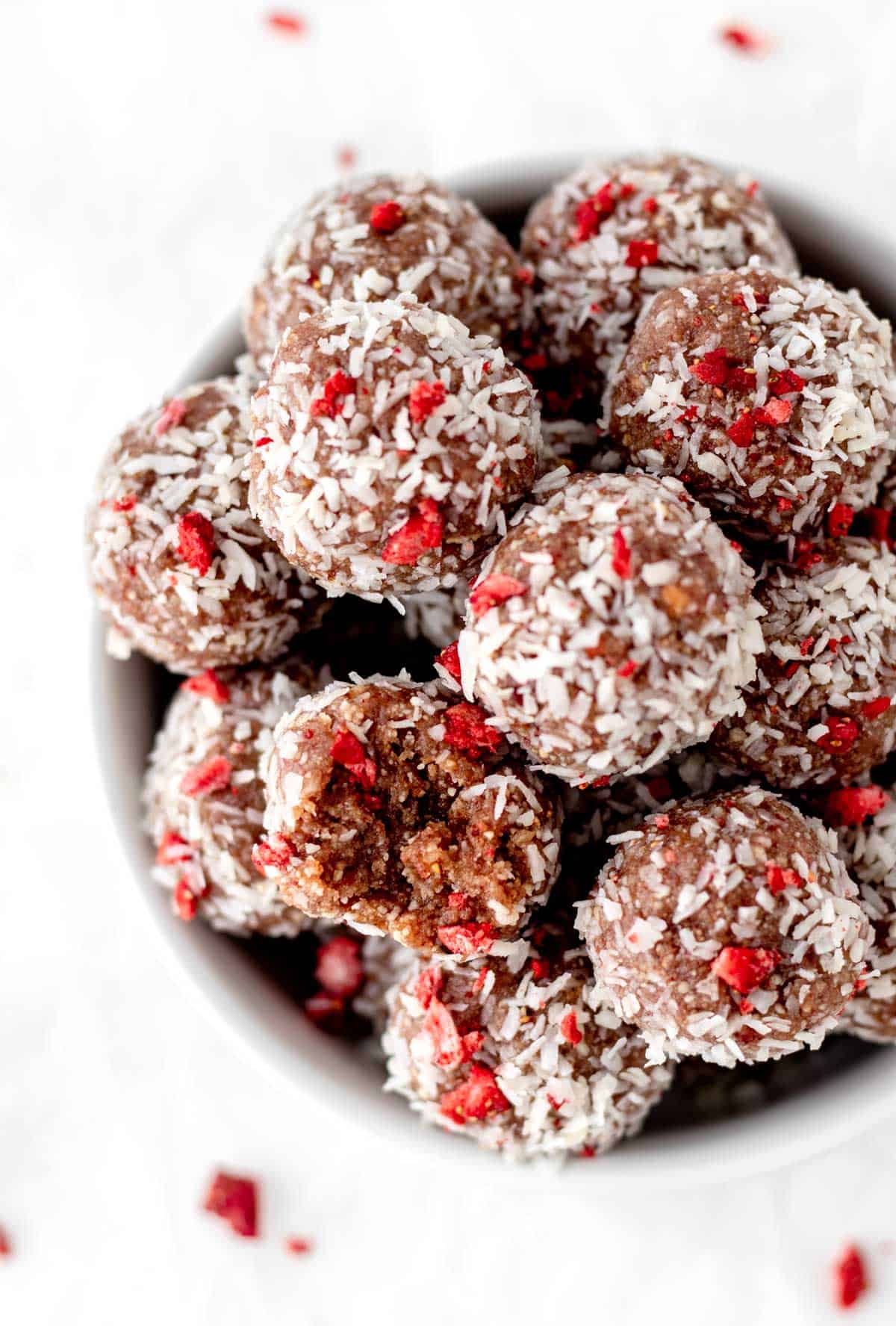 A birds-eye view of strawberry bliss balls in a glass bowl, with one half-bitten.