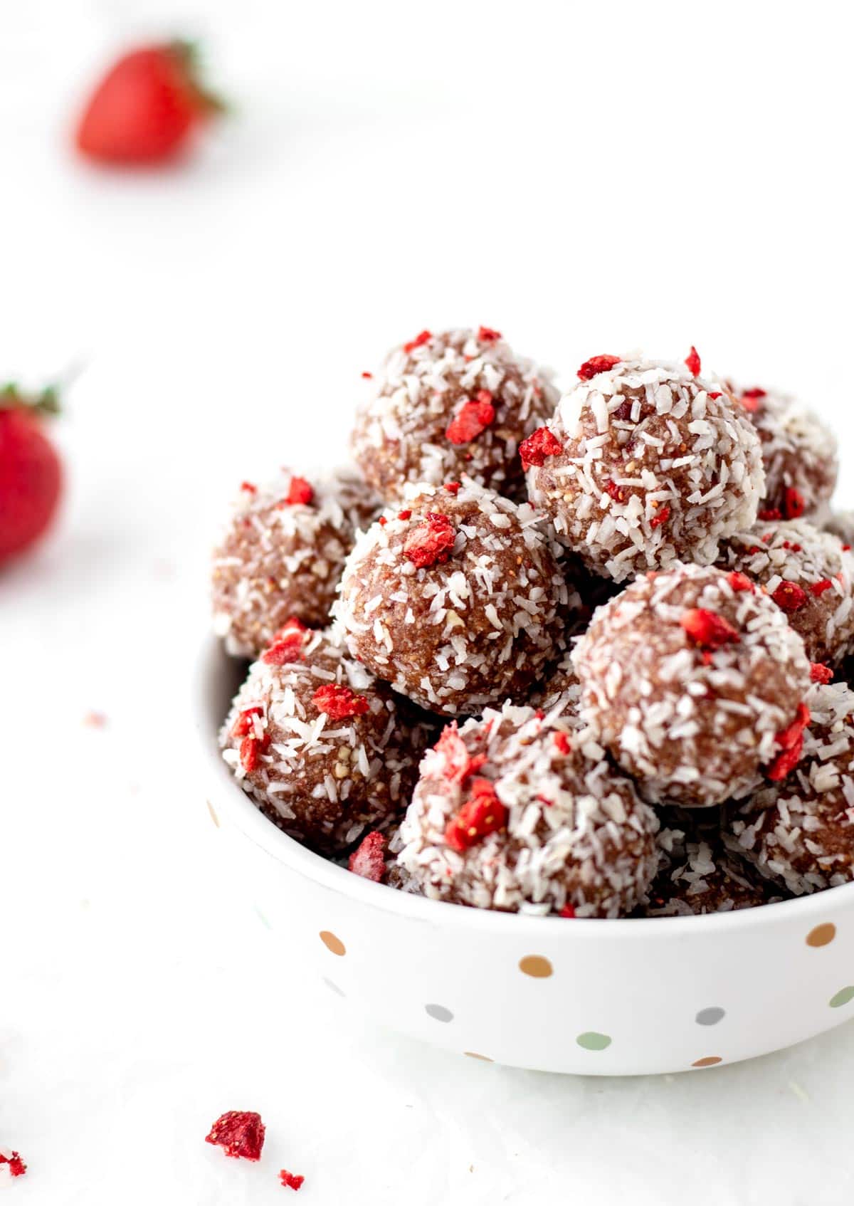 Strawberry energy balls in a polka dot bowl on a counter.