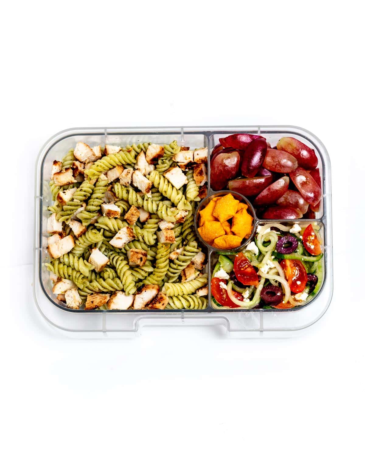 A veggie lunchbox idea featuring pasta salad, grapes, a cucumber noodle salad and crackers.