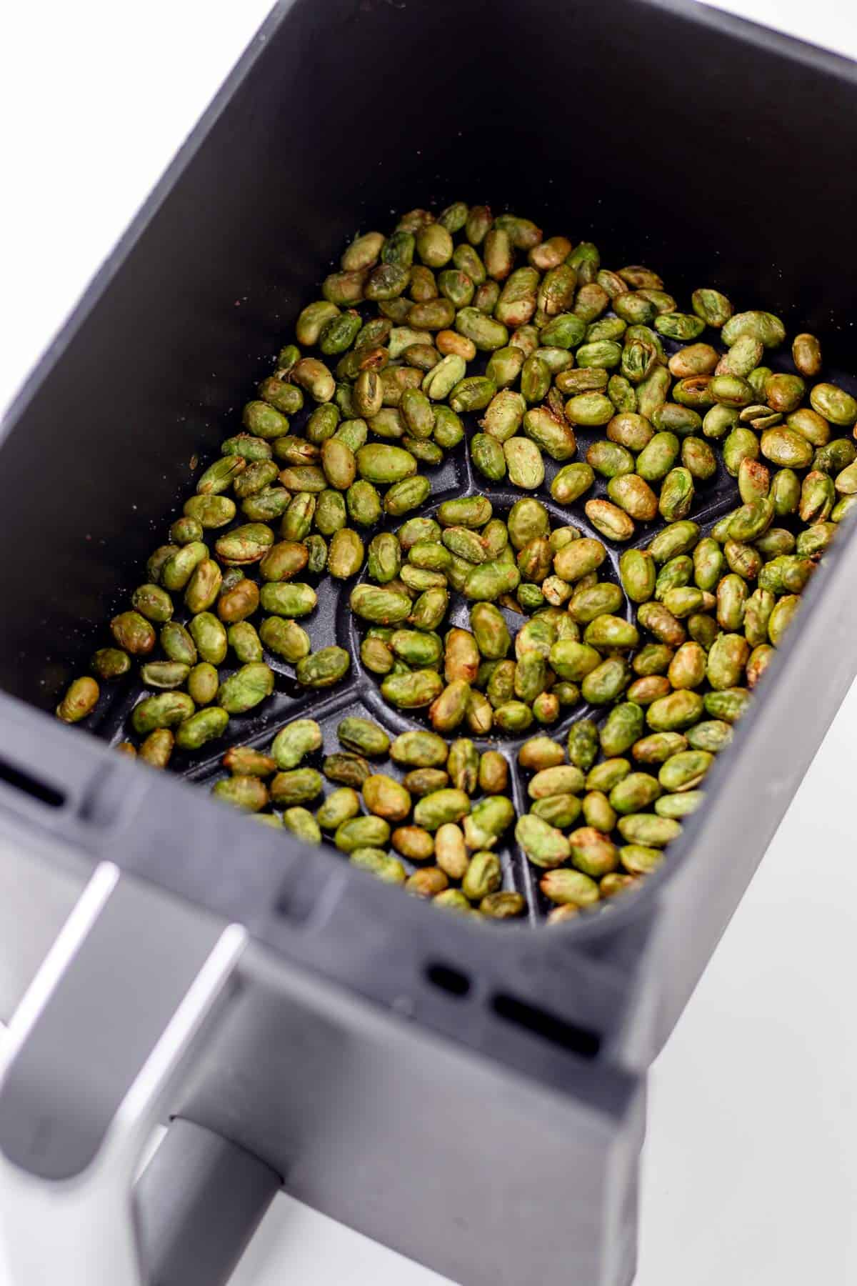 A fried edamame in an air fryer basket.