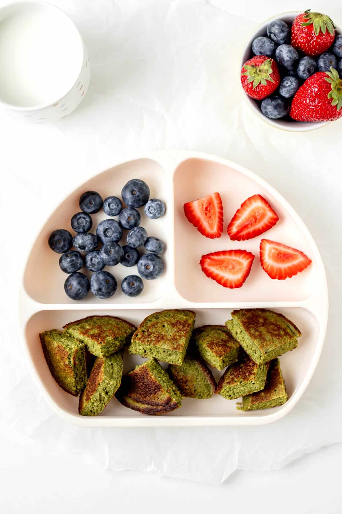 A divided plate with hulk pancakes, strawberries and blueberries.