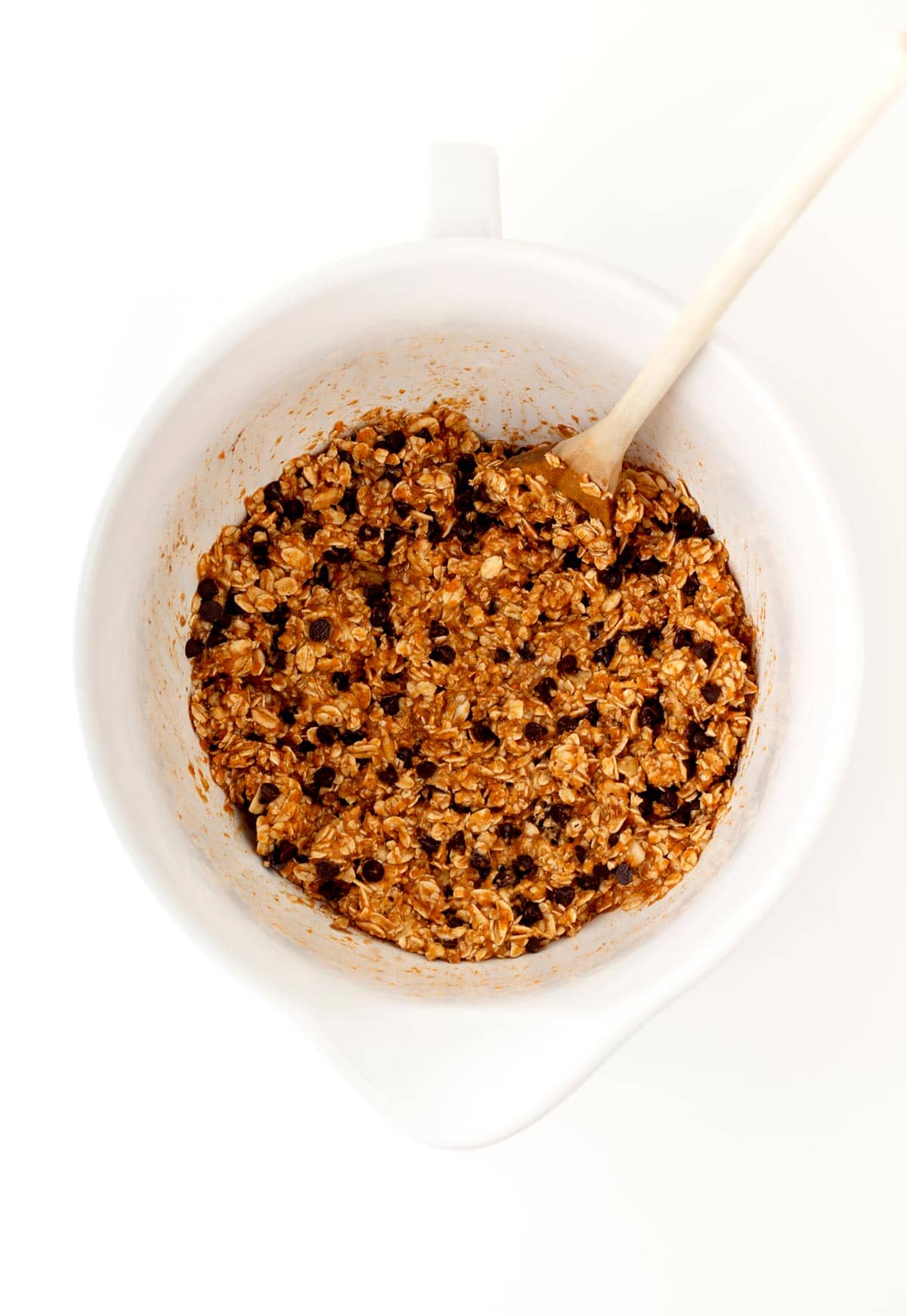 The banana pumpkin cookie mixture combined in a bowl with a wooden spoon in it.