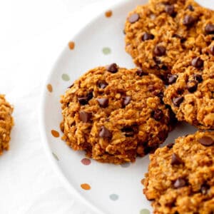 A close up image of pumpkin banana cookies stacked on a polka dot plate.