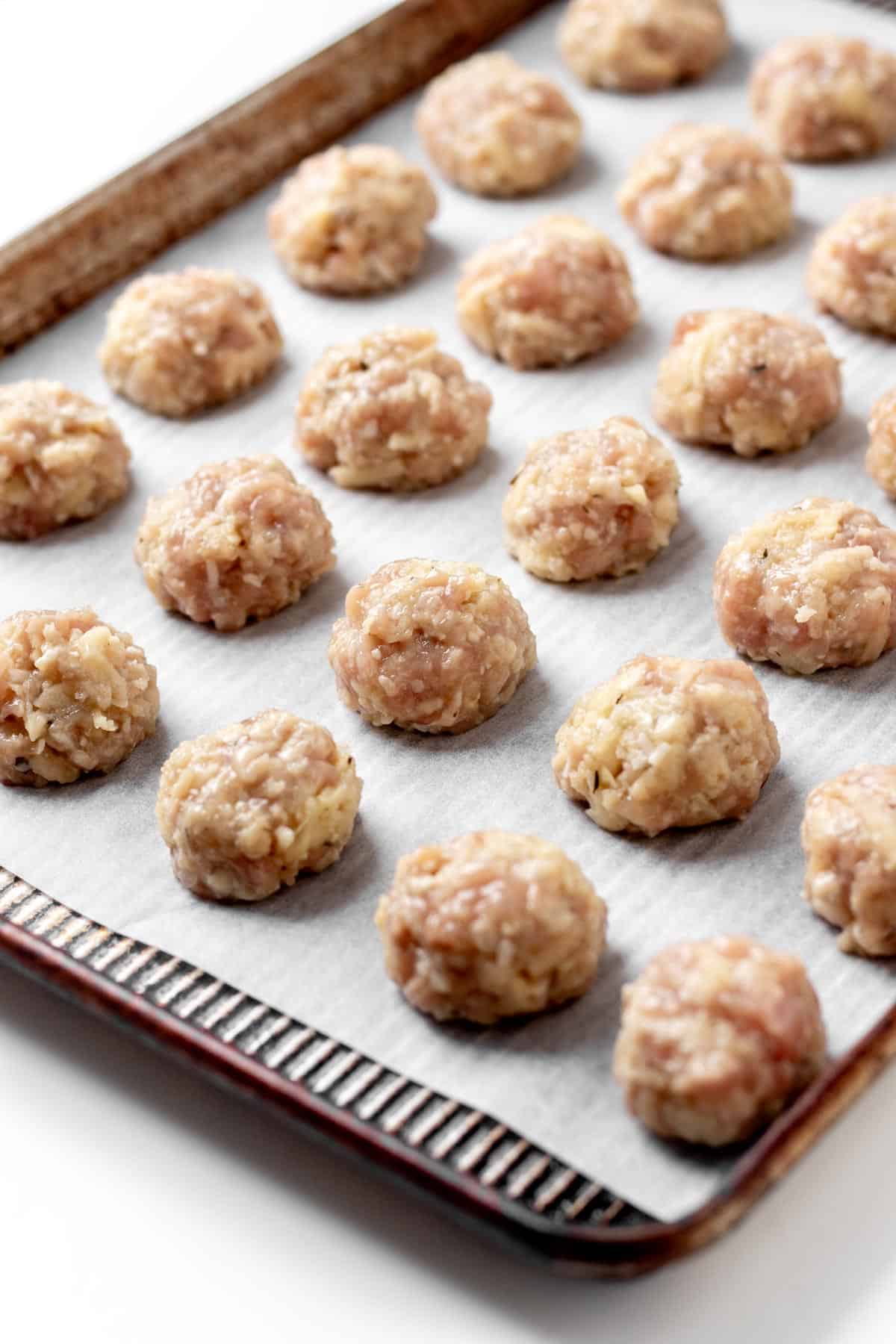 Raw apple and chicken meatballs on a parchment paper lined baking sheet.