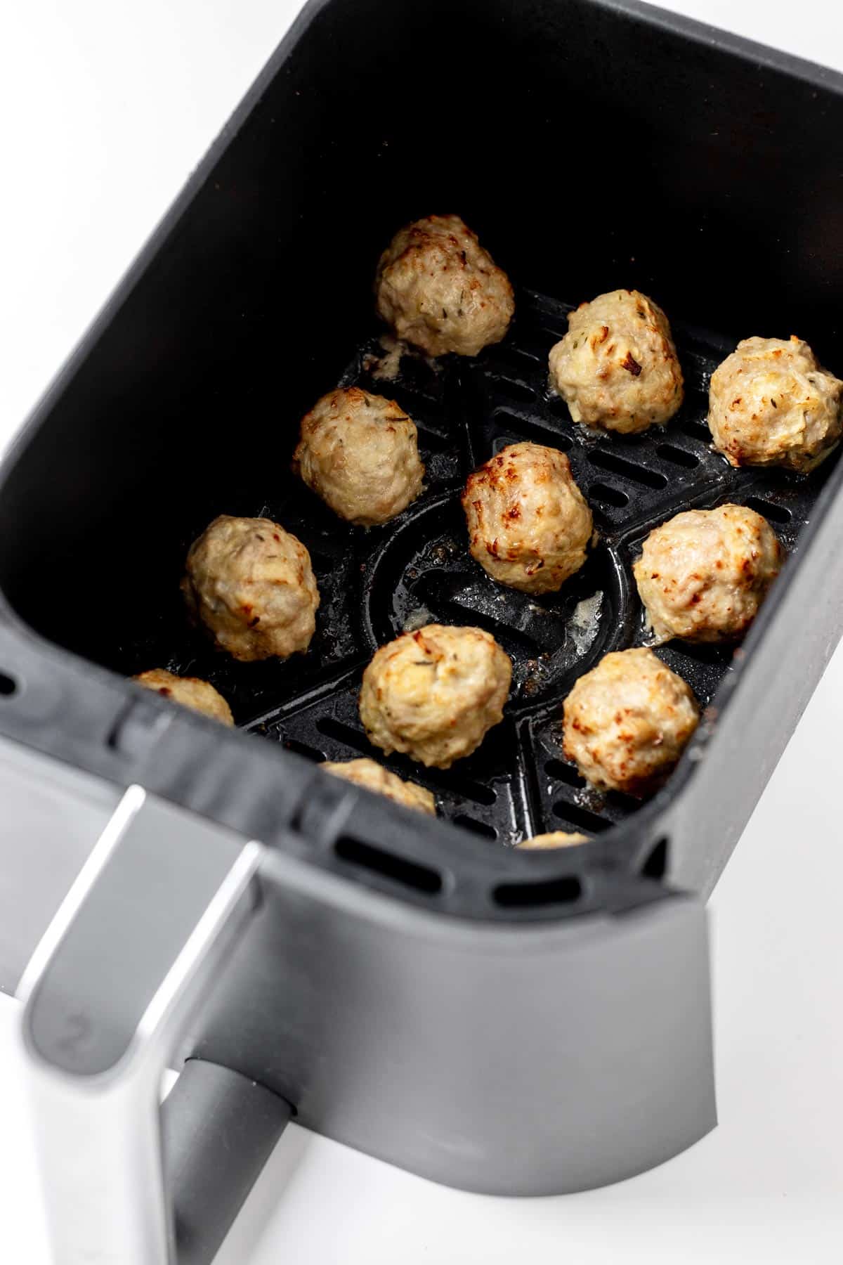 Apple and chicken meatballs in an air fryer basket.