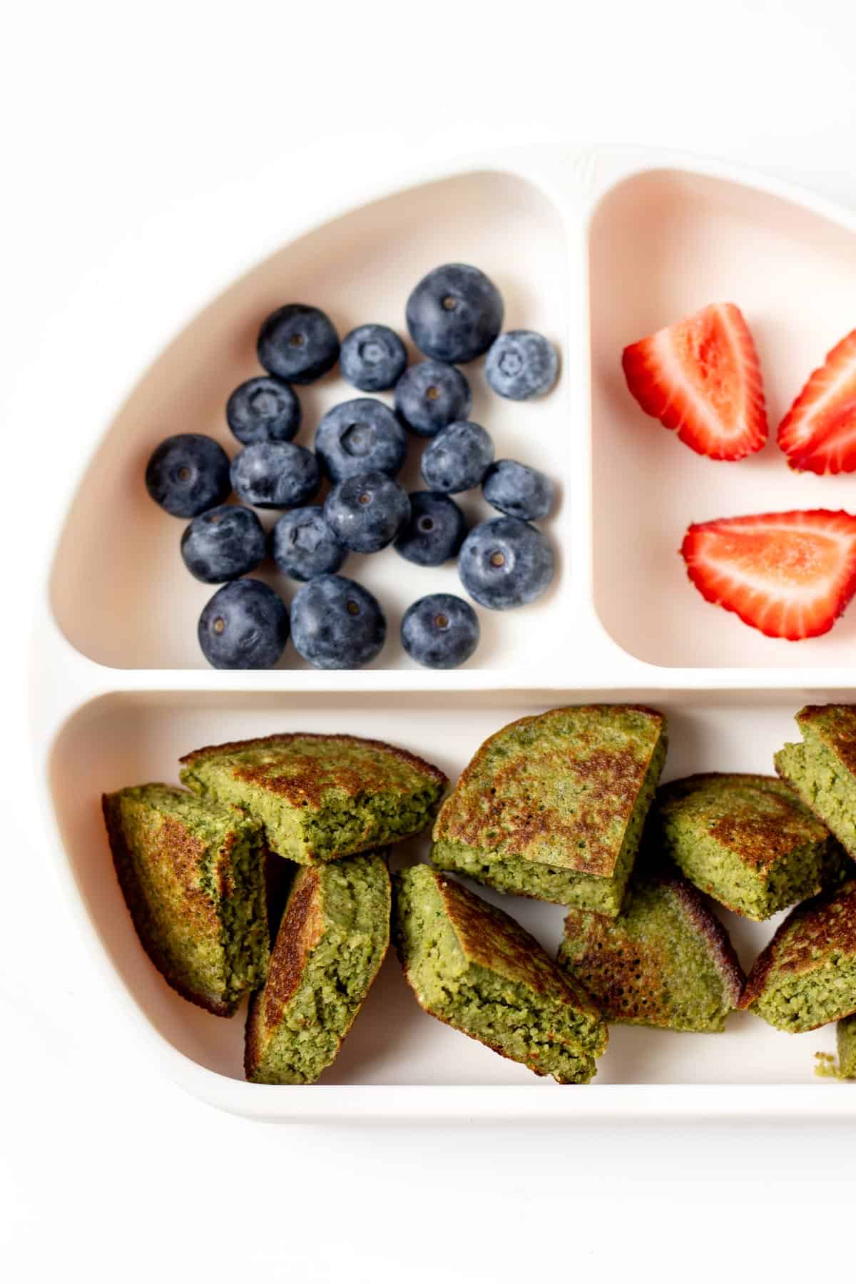 A close-up of the hulk pancakes, strawberries and blueberries on a divided plate.