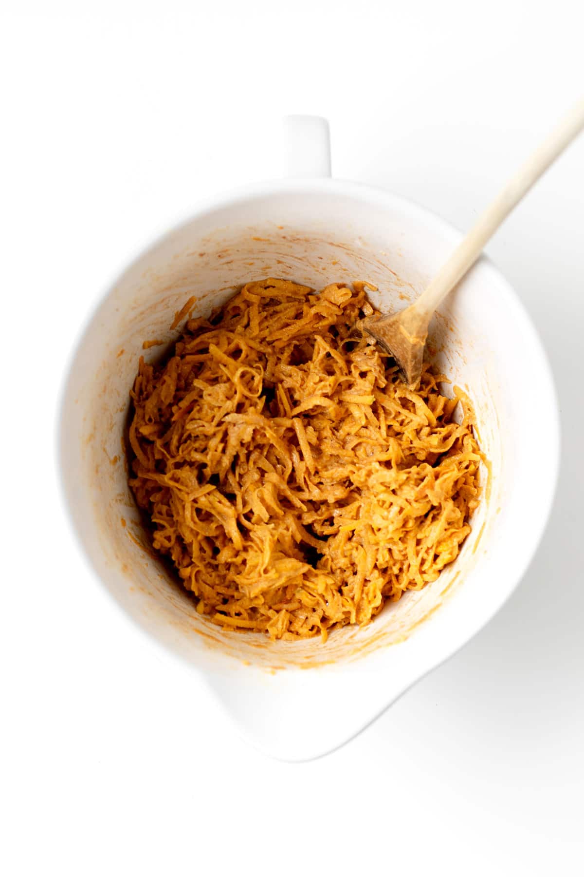 The shredded butternut squash mixture in a white mixing bowl with a wooden spoon.