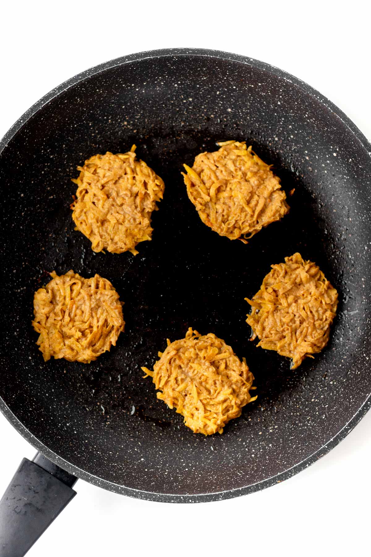 Cooking the butternut squash cakes in a frying pan on the stove.