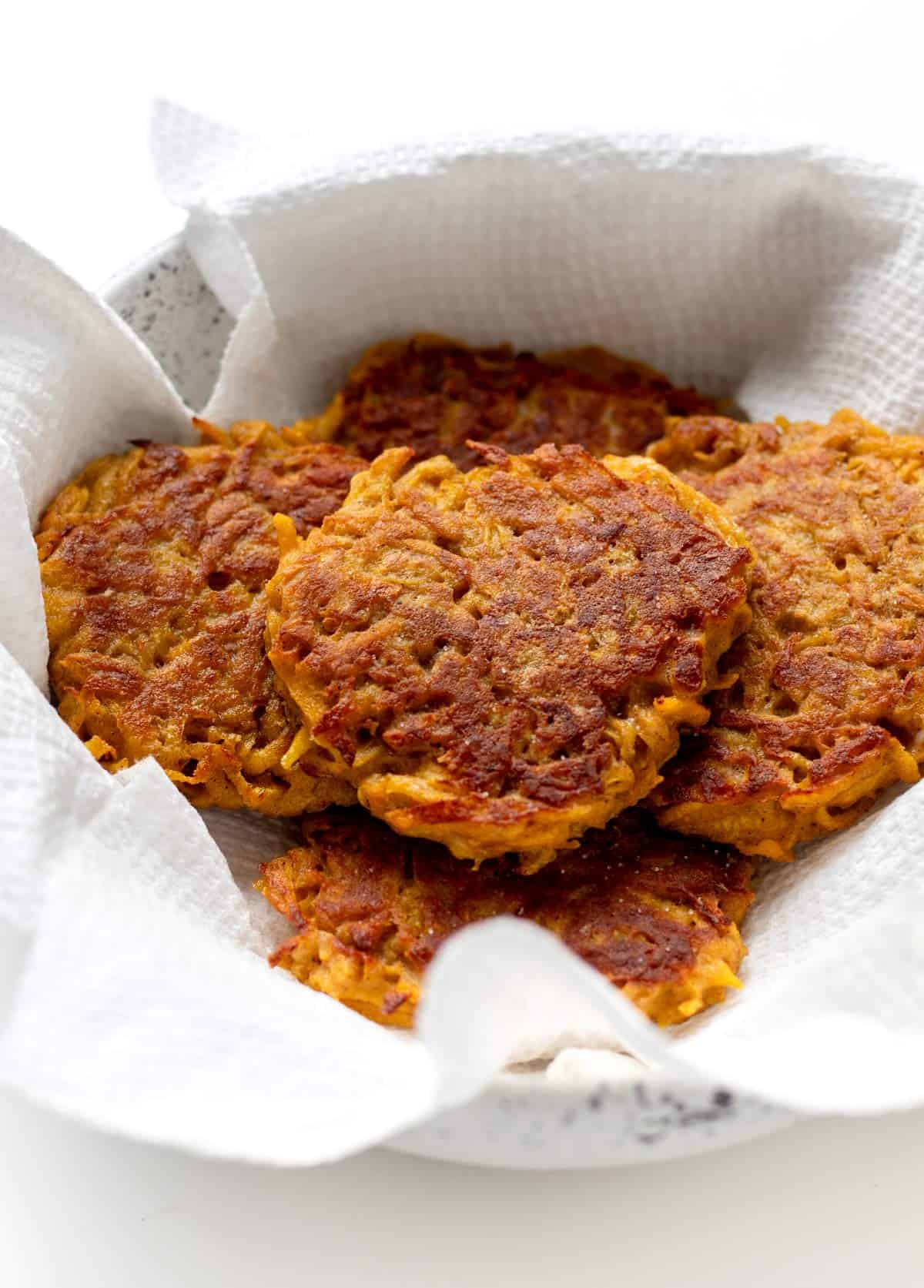 Crispy butternut squash cakes in a towel-lined bowl.